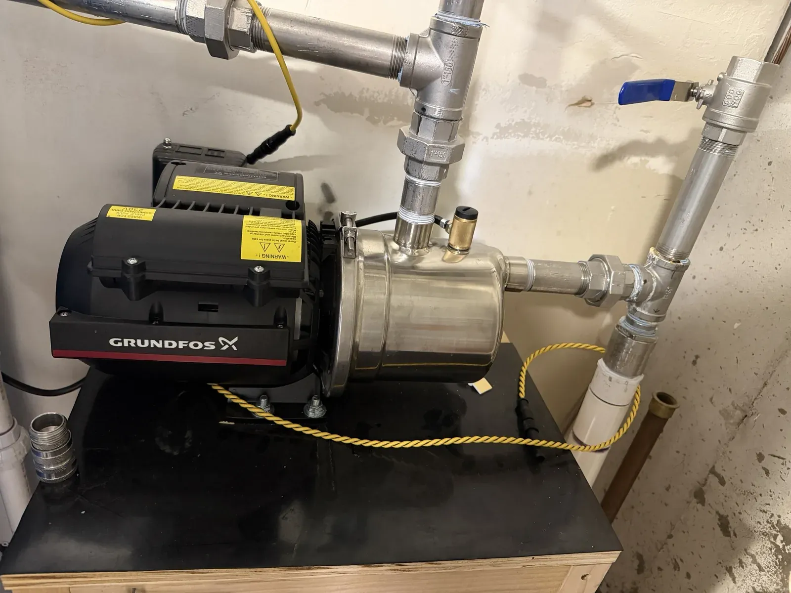 A Grundfos booster pump on a plywood stand with the sensor's rope looped around its body