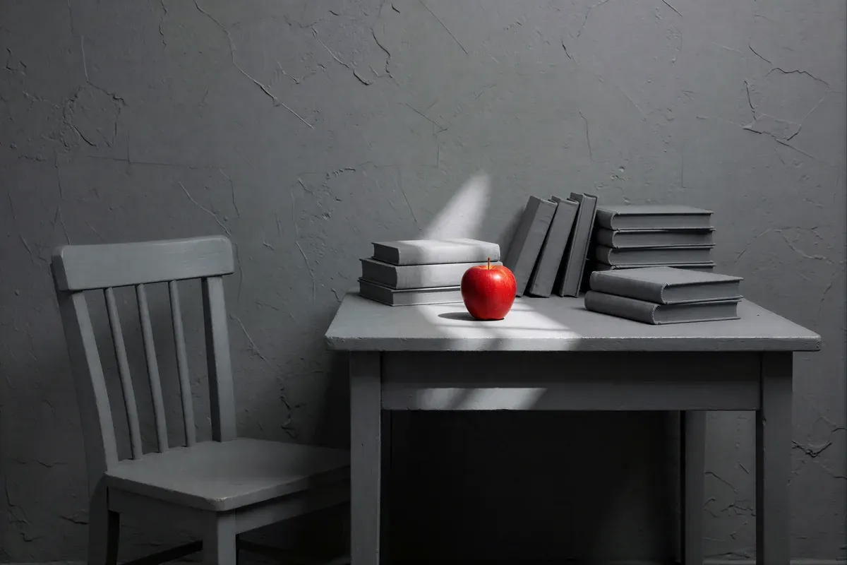 A grey room with a grey chair, grey books and one red apple on the table