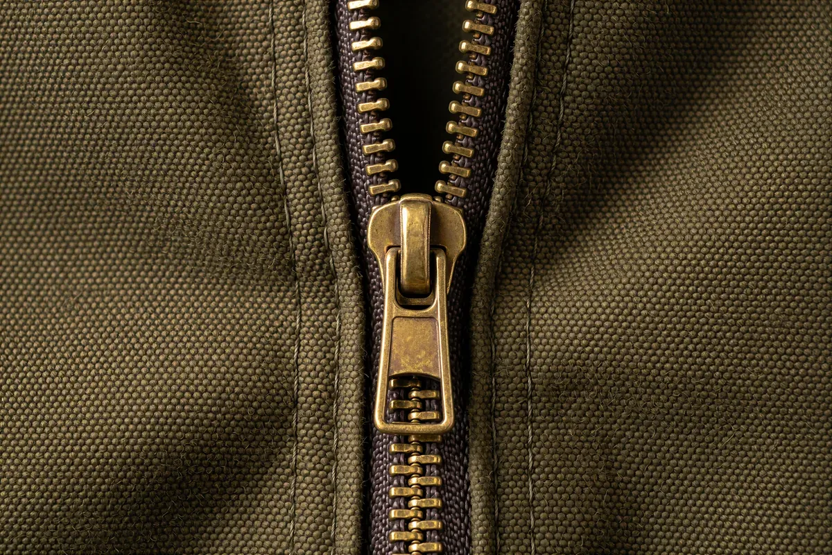 A brass zipper half open on olive waxed canvas